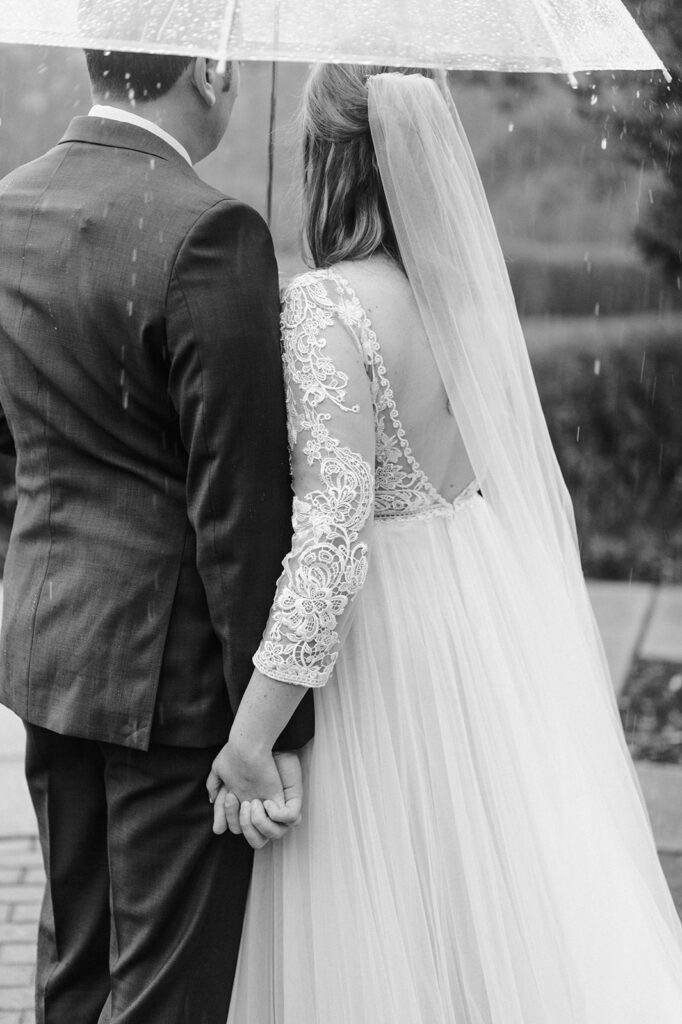 Bride and Groom hold hands in the rain under an umbrella